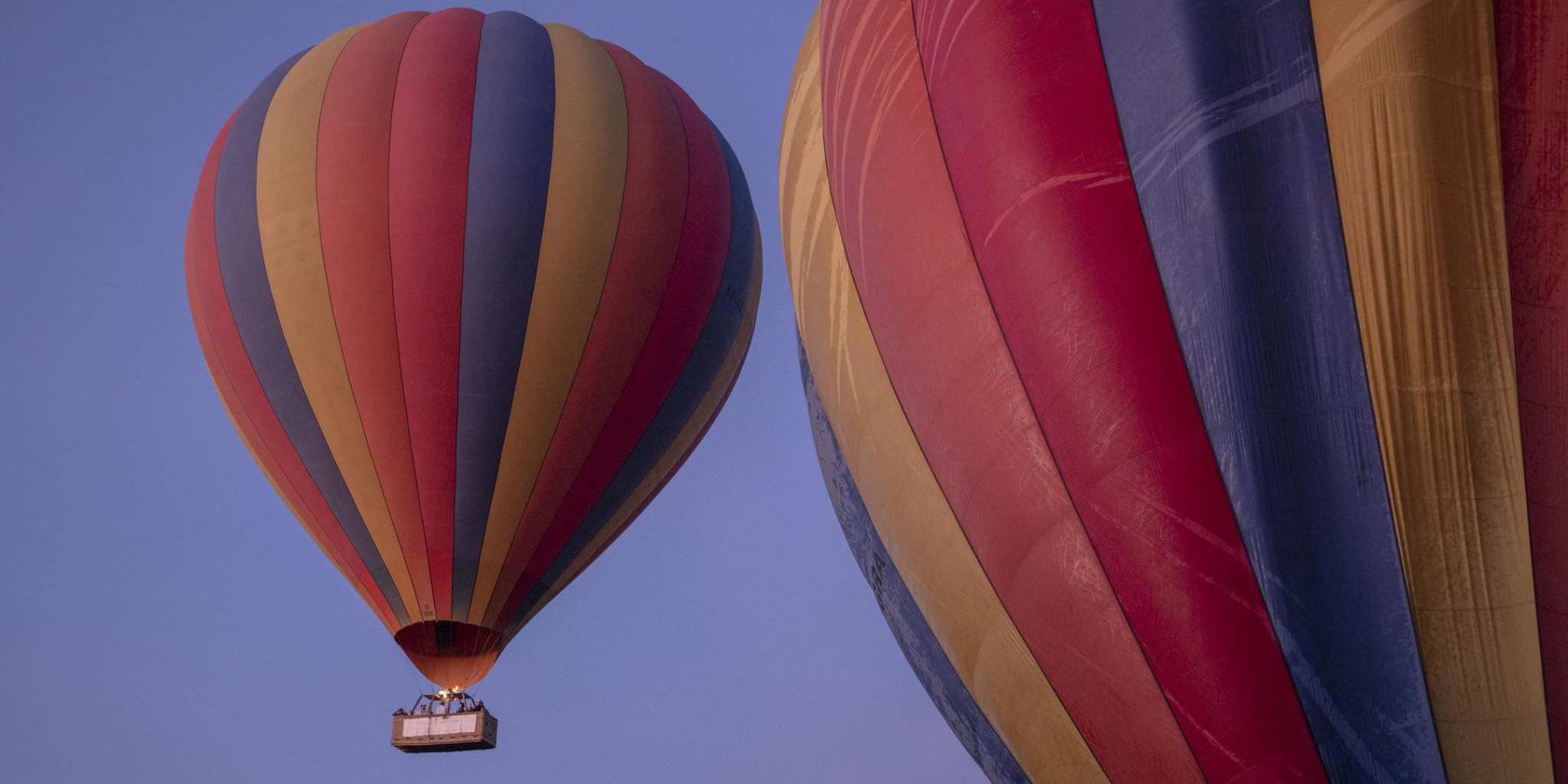 Two rainbow hot air balloons ascending into the sky at sunrise