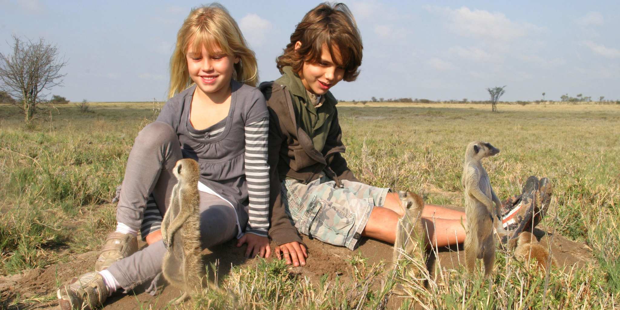 Two children playing with meerkats in the grass
