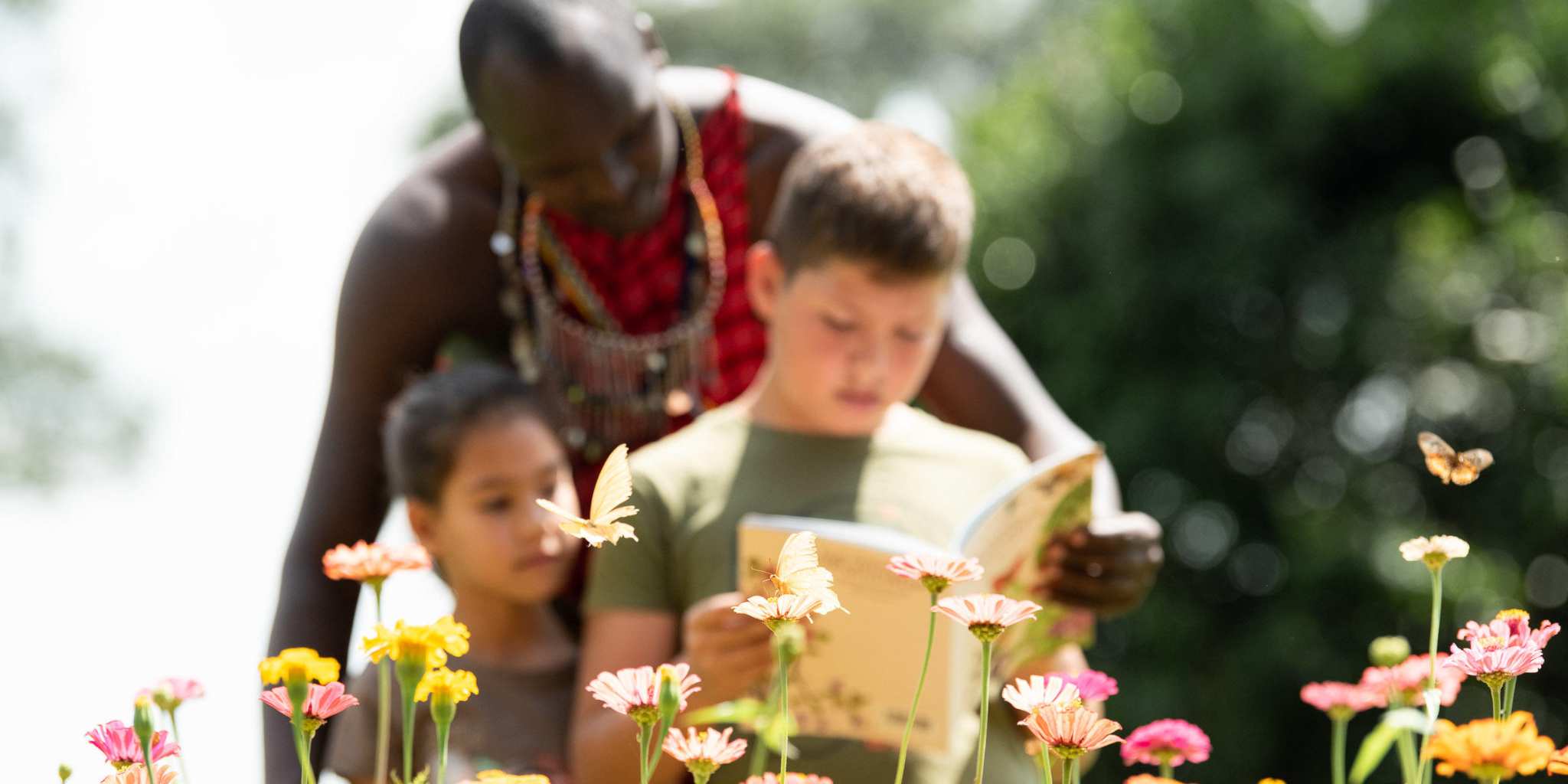 Two children and a guide reading surrounded by colourful flowers