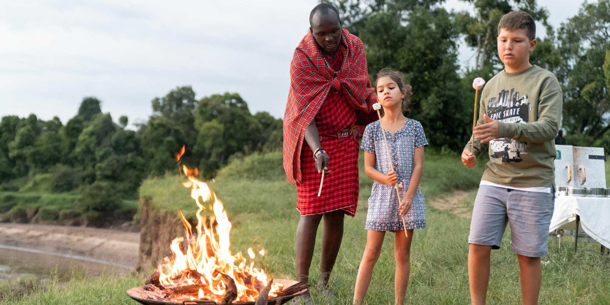 A guide and two children enjoying marshmallows around a campfire.