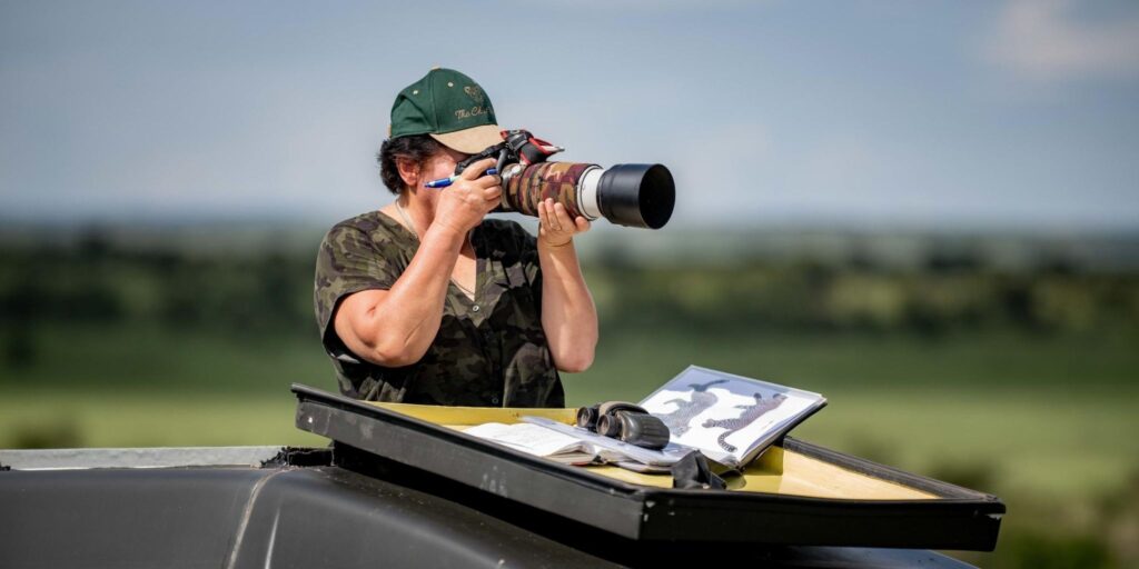 A woman standing in a safari vehicle using a camera