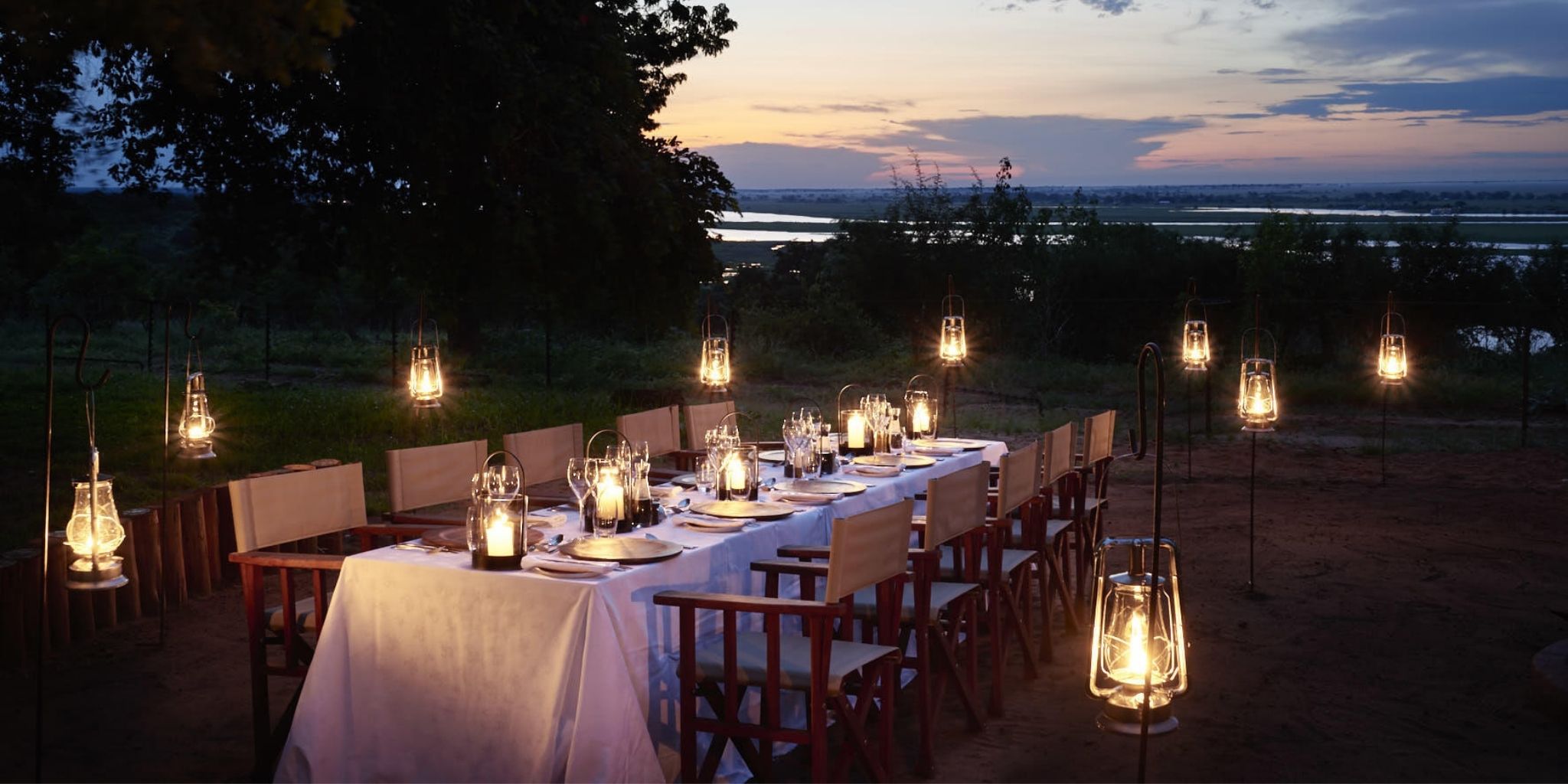 Table beautifully made up for a group dining experience at sunset, lit up by candles and latterns