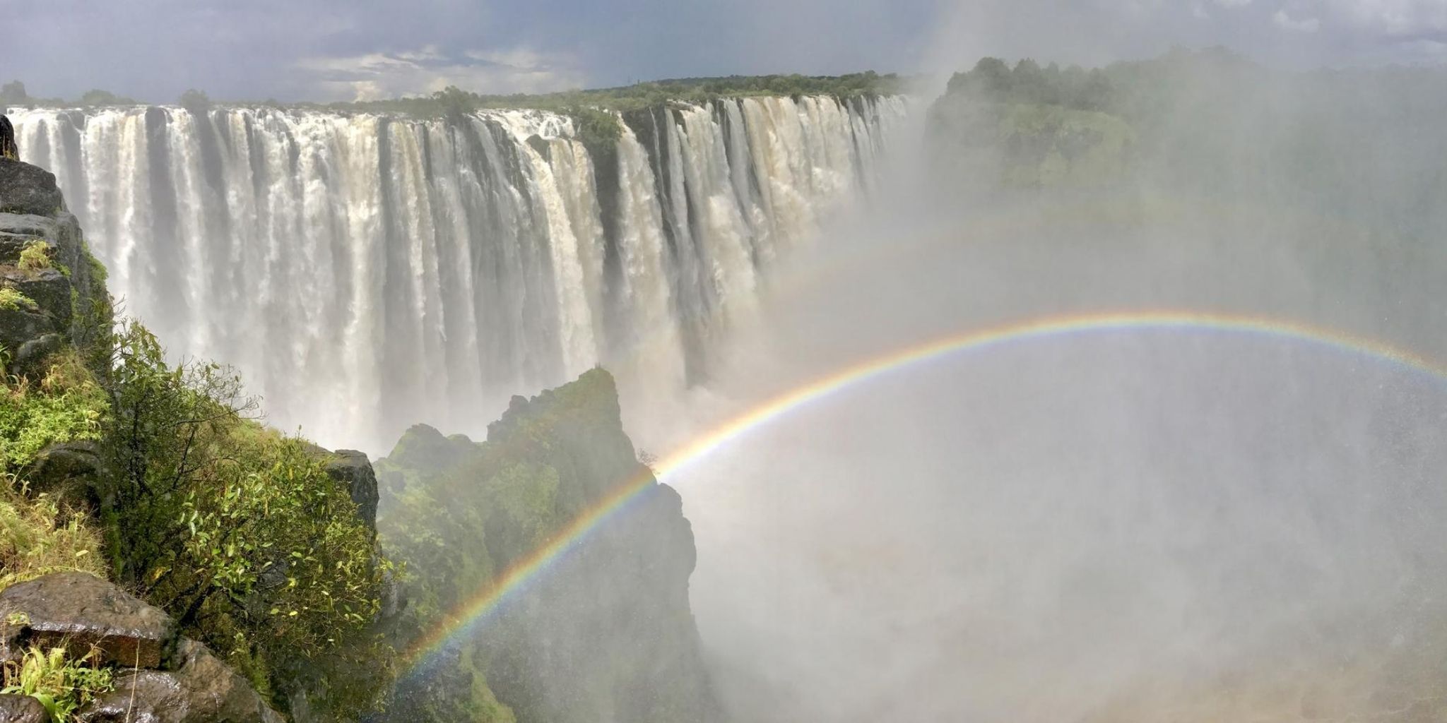 Stunning view of Victoria Falls in peak season wiht a rainbow in the foreground