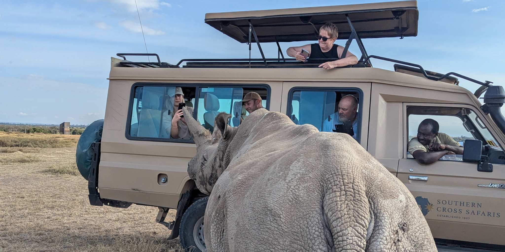 Rhino standing very close to a safari vehicle with people in all trying to capture a picture of it